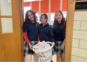 3 girls in school uniforms holding a basket and smiling at the camera